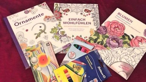Farbenfrohe Malbücher für Erwachsene liegen auf einem roten Samtuntergrund, umgeben von Buntstiften.