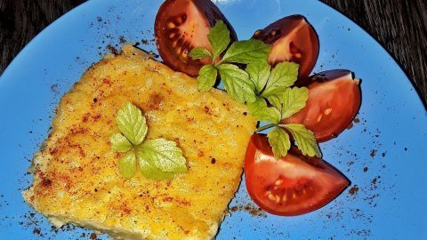 Ein Stück Karanteta liegt auf einem blauen Teller, umgeben von frischen Tomatenscheiben und grüner Minze.