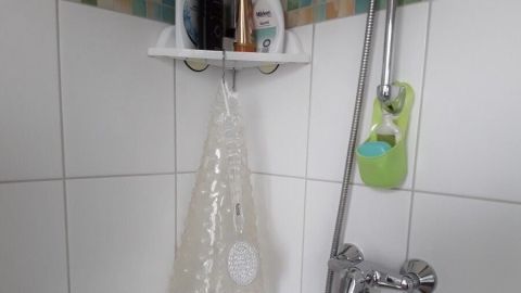 Eine Duschmatte hängt feucht in der Dusche, während Duschgel und Pflegeprodukte in einem Regal an der Wand stehen.