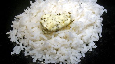Weißer Reis mit Kräuterbutter liegt dekorativ auf einem schwarzen Teller und wartet darauf, serviert zu werden.
