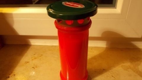 Eine rote Grableuchte steht auf einem Tisch, geschützt durch einen Deckel, im Innenbereich vor Nässe.