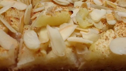 Ein saftiger Apfelkuchen ohne Zuckerzusatz liegt auf einem Teller, garniert mit mandelnden Scheiben, in einer hellen Küche.
