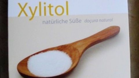 Eine Verpackung mit Xylit zeigt einen Holzlöffel, der weißen Zuckeraustauschstoff hält, auf einem neutralen Hintergrund.