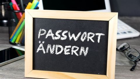 Ein kleines Holzschild mit der Aufschrift „PASSWORT ÄNDERN“ steht auf einem Tisch mit Büroelementen im Hintergrund.