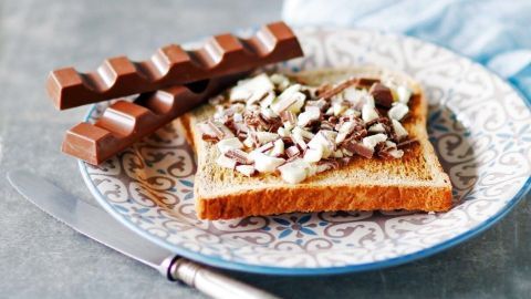 Ein Stück Toast liegt auf einem Teller und ist mit zerkleinerter Kinderschokolade dekoriert, daneben liegen mehrere Riegel.