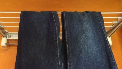 Zwei Hosen hängen ordentlich an einer Wäscheleine ohne Klammern, auf einem hellen Hintergrund, zum Trocknen.