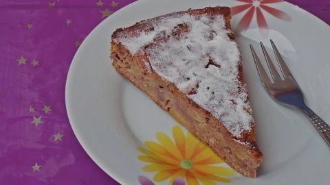 Ein Stück Apfelkuchen mit Kastanienmehl und Eiweißpulver liegt auf einem blumengemusterten Teller auf einem lila Tisch.