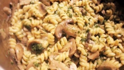 Ein Topf mit spiralförmigen Nudeln, Champignons und Spinat wird in der Küche zubereitet, vegetarisches Gericht.