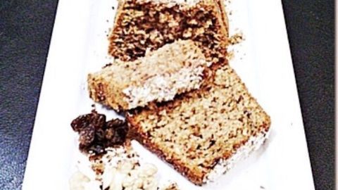 Ein saftiger Dattel-Mandel-Walnusskuchen liegt auf einem weißen Teller, mit einigen Stücken daneben und Nüssen drumherum.