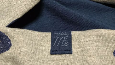 Ein beiges Textil mit glitzerndem Lippenmuster zeigt das Etikett „made by Me“ im Inneren, das Individualität ausdrückt.