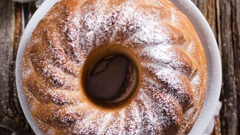 Ein saftiger Marmorkuchen auf einem weißen Teller, umgeben von rustikalem Holz, mit Puderzucker bestäubt.
