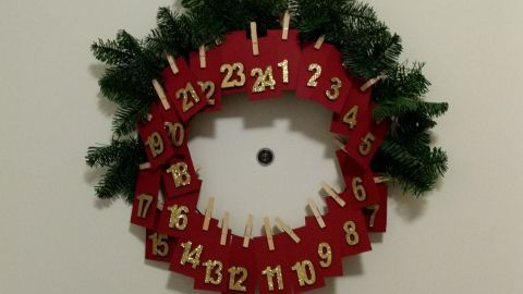 Ein Adventskalender in Form eines Türkranzes hängt dekorativ an der Wand und zeigt 24 nummerierte Türchen, umrahmt von Tannenzweigen.