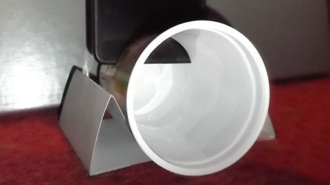 Ein Handy steht in einem selbstgemachten Lautsprecher aus einem Becher, der den Klang verstärkt und auf einer Halterung steht.