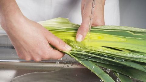 Frische Lauch wird unter fließendem Wasser gereinigt, um Gewürze und Kräuter für Soßen oder Suppen vorzubereiten.