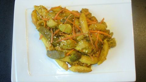 Schupfnudeln sind auf einem weißen Teller mit asiatisch inspiriertem Gemüse und Gewürzen angerichtet, in einer dunklen Umgebung.