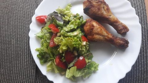Zarte Hähnchenunterkeulen liegen neben einem frischen, bunten gemischten Salat auf einem weißen Teller.