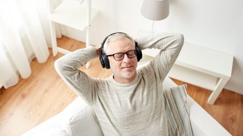 Ein Mann sitzt entspannt auf einer Couch, trägt Kopfhörer und genießt die ruhige Atmosphäre des sonnigen Raums.