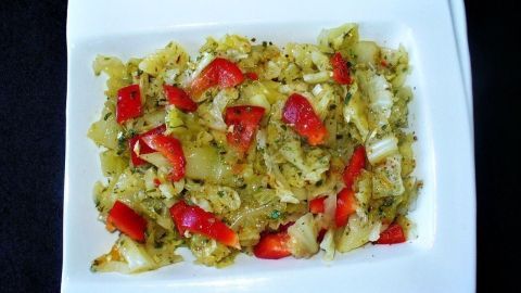 Warmer Weißkohlsalat mit roten Paprikastücken liegt auf einem weißen Teller und wirkt frisch in einem dunklen Umfeld.