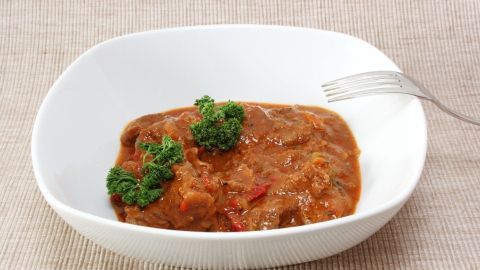 Ein zarter Szegediner Gulasch wird in einer weißen Schüssel serviert, garniert mit frischer Petersilie auf einem neutralen Hintergrund.