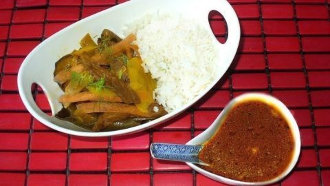 Ein Gericht mit Rindfleischstreifen, Gemüse und Reis in einer weißen Schüssel, begleitet von einer kleinen Schale Sauce.