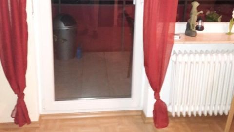Rote Vorhänge rahmen eine Glastür, die zu einem Balkon führt, in einem gemütlichen Wohnraum mit Holzboden.