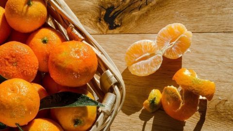 Frische Mandarinen liegen in einem Korb, während einige auf einem Holztisch aufgeschnitten sind, ideal für Snacks oder Deko.