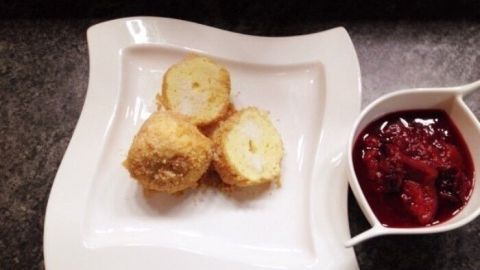 Drei goldene Quarkknödel liegen auf einem eleganten Teller neben einer Portion Zwetschgenröster in einer weißen Schale.
