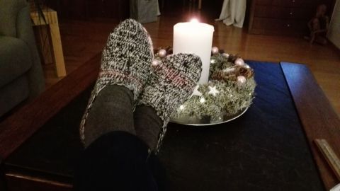Gestrickte Haus- oder Bettsocken liegen entspannt auf einem Tisch neben einer brennenden Kerze in einer gemütlichen Umgebung.