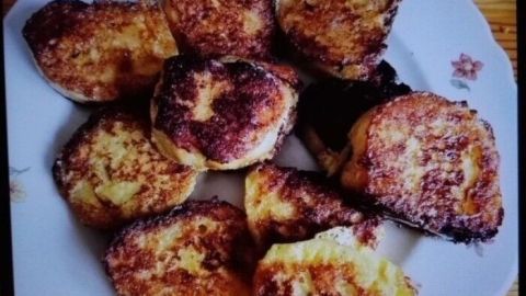 Auf einem weißen Teller liegen braun gebratene Dampfnudeln, die appetitlich angerichtet sind, umgeben von einem Holzuntergrund.