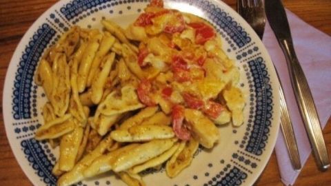 Ein Teller zeigt eine appetitliche Scharfe Paprika-Hähnchen-Pfanne mit Capunti, angerichtet mit rotem Gemüse, auf einem rustikalen Tisch.