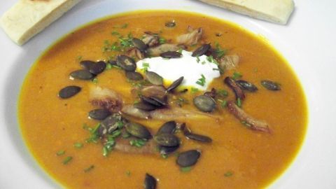 Eine cremige Kürbissuppe mit gebratenen Austernpilzen und einem Klecks Sahne, umgeben von Brotstücken.