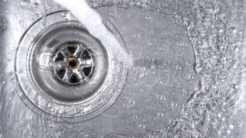 Ein glänzender Abfluss wird von Wasser umspült, während es im Spülbecken abfließt, was die regelmäßige Pflege verdeutlicht.