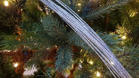 Eine silberne Geschenkbandrolle liegt über einem geschmückten Weihnachtsbaum mit leuchtenden Lichtern umgeben.