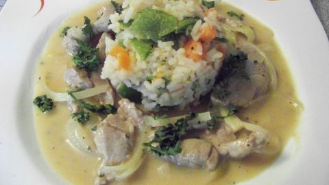 Schweinelende in cremiger Sauce umgeben von buntem Gemüsereis, appetitlich angerichtet auf einem weißen Teller.