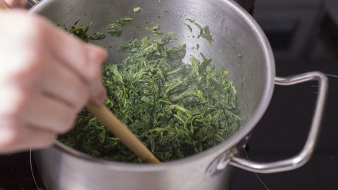Kochendes Grünkohl wird in einem Topf mit einem Holzlöffel umgerührt, um ein leckeres vegetarisches Gericht zu zaubern.