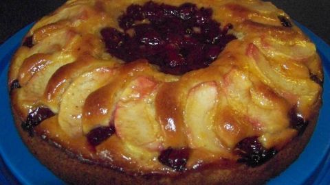 Ein saftiger Apfel-Kirsch-Kuchen liegt auf einem blauen Teller, umgeben von einer warmen Küchenatmosphäre.