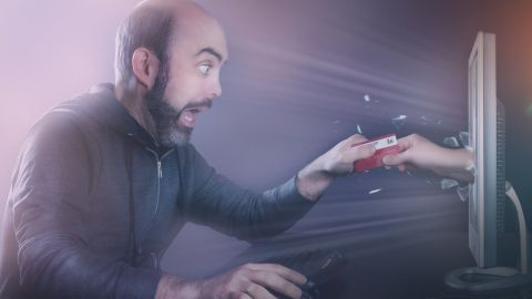 Ein Mann sitzt vor einem Computer und greift überrascht nach einem Geldschein, der von einem Bildschirm reicht.