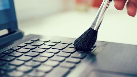 Ein Pinsel reinigt die Tastatur eines Laptops, um PC-Teile und die Tastatur staubfrei zu bekommen, in einer hellen Umgebung.