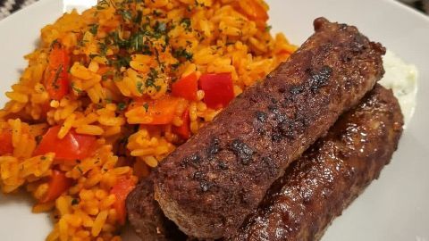 Zwei saftige Hackfleischröllchen liegen neben bunter, würziger Reisbeilage auf einem Teller, appetitlich angerichtet.