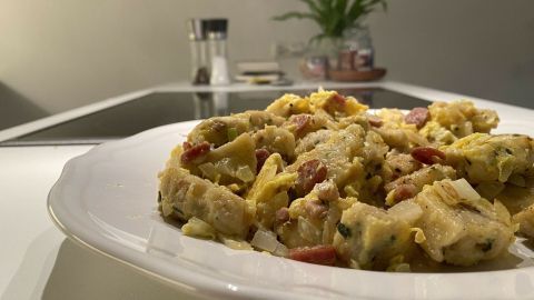 Geröstete Knödel liegen auf einem weißen Teller, umgeben von einer modernen Küche mit Pflanzen im Hintergrund.