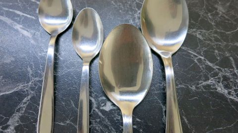 So entfernt man Rost von Silberlöffeln: Einfach den Löffel so lange ins Wasser mit ca. 1 Löffel Melkfett legen, bis der Rost sich leicht abkratzen lässt oder sich von selbst löst. Vier glänzende Silberlöffel liegen auf einer dunklen Marmoroberfläche, bereit zur Pflege gegen Rost mit Melkfett.