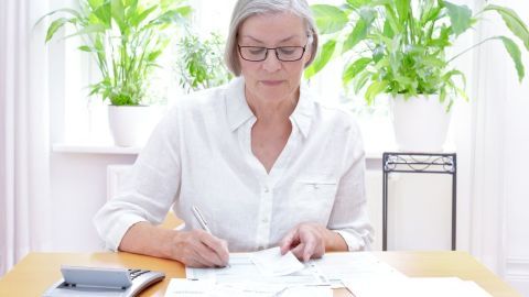 Eine Frau sitzt an einem Tisch und überprüft Belege für die Steuererklärung, um sie auf Anfrage zu sortieren.