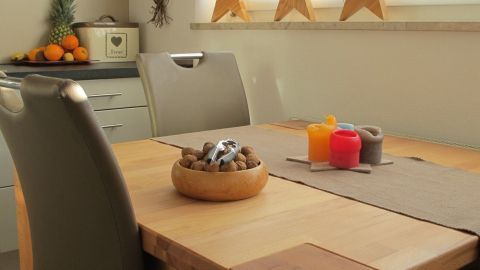 Ein Holztisch mit einem dekorativen Behälter und Kerzen steht in einem hellen Raum, umgeben von Küchenaccessoires und Sternen.