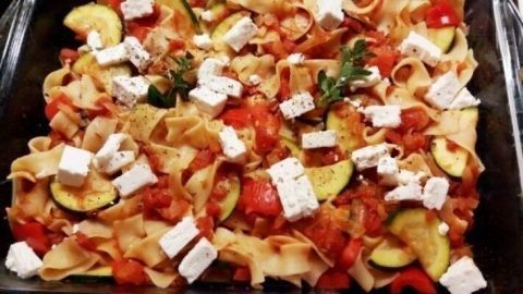 Nudelauflauf mit Schafskäse liegt heiß in einer Auflaufform, garniert mit Zucchini und Tomatenstücken.