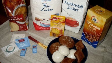 Zwei Tüten Zucker und weitere Zutaten liegen auf einem Tisch, während Eier und Snacks in einer Schüssel arrangiert sind.