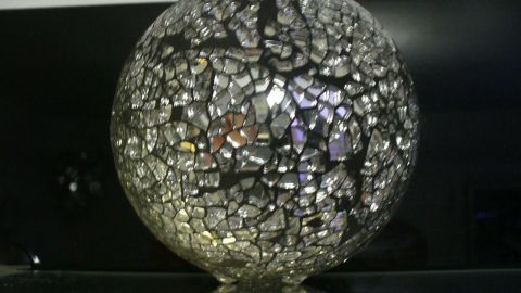Eine runde Deko-Kugel steht glänzend auf einer dunklen Oberfläche und reflektiert das Licht durch ihre glitzernde Oberfläche.