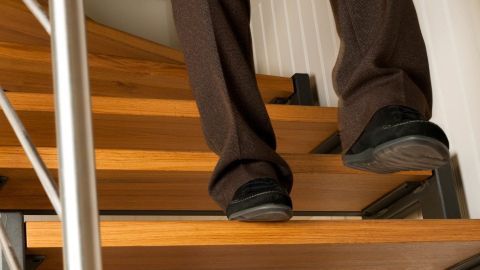 Eine Person in dunkler Kleidung steht auf einer Treppe, während sie hinabgeht, vermutlich mit Knie- und Gelenkproblemen.