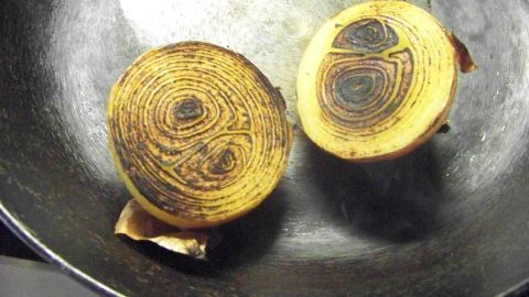 Zwei angebratene Zwiebelhälften liegen in einer Eisenpfanne, die auf einer sauberen Kochstelle platziert ist.