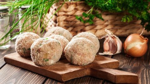 Saftige Frikadellen liegen auf einem Holzbrett, umgeben von frischen Kräutern und Zwiebeln in einer gemütlichen Küche.