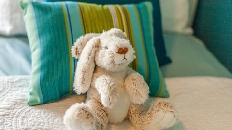 Ein weicher Hase sitzt auf einem Bett, umgeben von bunten Kissen, ideal für Kuscheltiere mit elektronischem Innenleben.